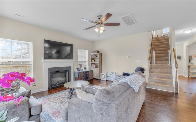 living room with a glass covered fireplace, stairway, wood finished floors, and visible vents