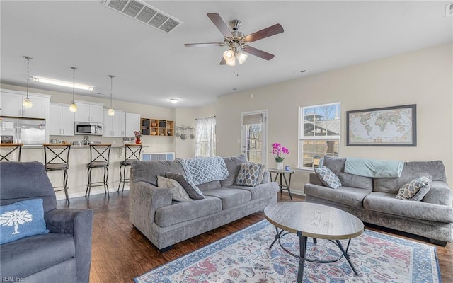 living room featuring dark wood-style flooring, visible vents, and a ceiling fan