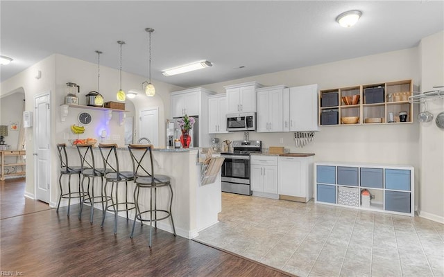 kitchen with a peninsula, white cabinetry, a kitchen breakfast bar, appliances with stainless steel finishes, and open shelves