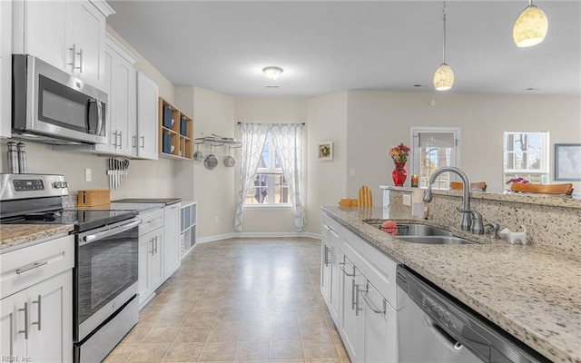 kitchen with light stone counters, pendant lighting, appliances with stainless steel finishes, white cabinets, and a sink