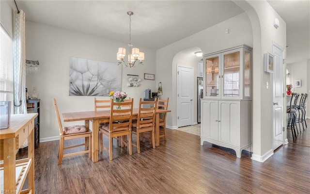 dining room featuring baseboards, arched walkways, a chandelier, and wood finished floors