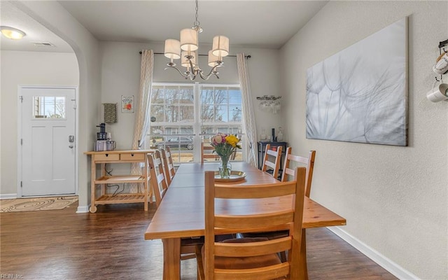 dining room with arched walkways, a chandelier, wood finished floors, visible vents, and baseboards