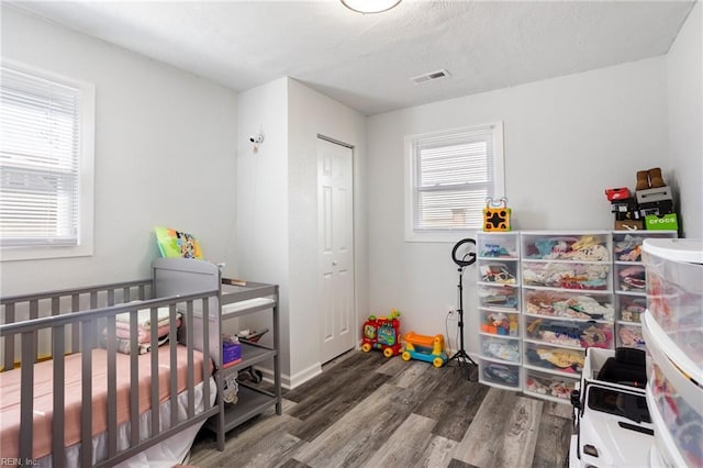 bedroom featuring a nursery area, a closet, visible vents, and wood finished floors