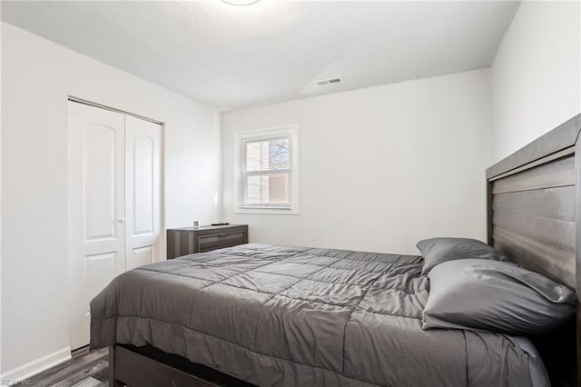 bedroom featuring baseboards, a closet, visible vents, and wood finished floors