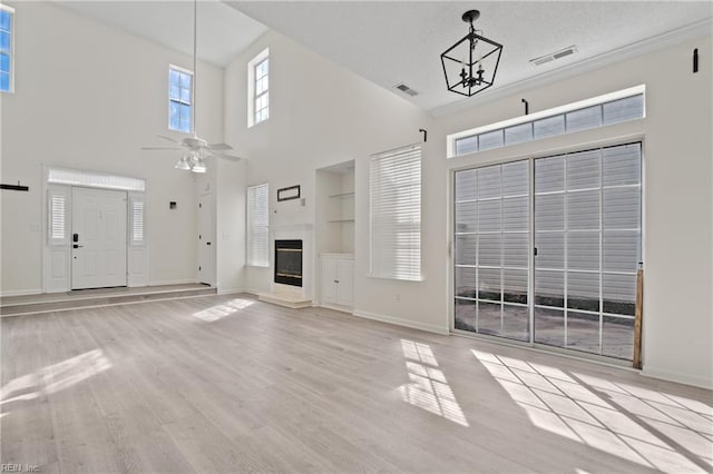 unfurnished living room featuring ceiling fan with notable chandelier, wood finished floors, a glass covered fireplace, and visible vents