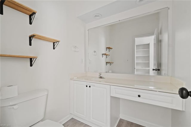 bathroom featuring toilet, baseboards, wood finished floors, and vanity