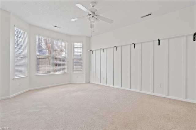 carpeted empty room featuring baseboards, ceiling fan, visible vents, and a textured ceiling