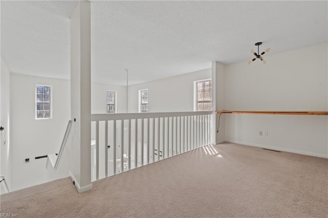 carpeted empty room with a notable chandelier, a textured ceiling, visible vents, and baseboards