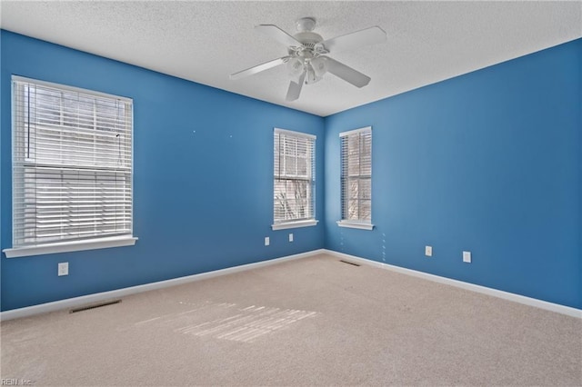 carpeted empty room featuring a ceiling fan, visible vents, baseboards, and a textured ceiling