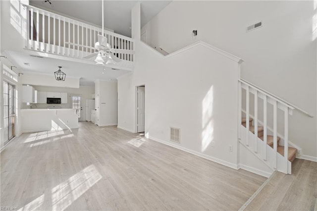 unfurnished living room with stairway, a towering ceiling, visible vents, and light wood-style floors