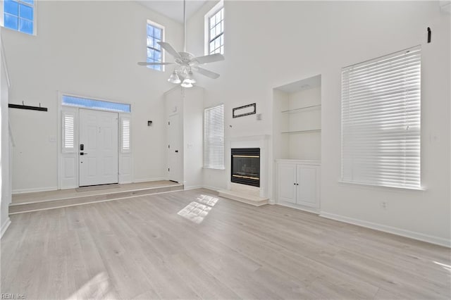 unfurnished living room with built in features, light wood-type flooring, a glass covered fireplace, and ceiling fan