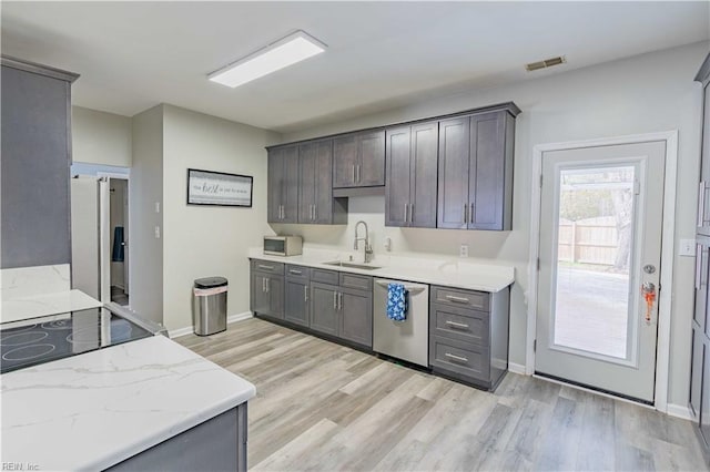 kitchen with light wood finished floors, baseboards, appliances with stainless steel finishes, light stone counters, and a sink