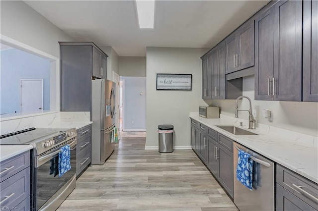 kitchen with baseboards, appliances with stainless steel finishes, light stone counters, light wood-style floors, and a sink