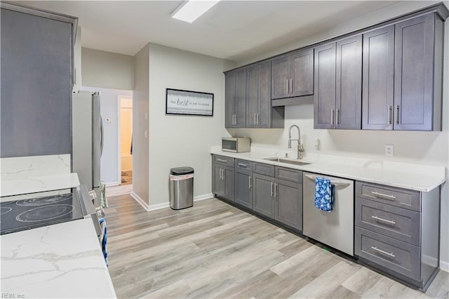 kitchen with stainless steel appliances, light wood-style floors, a sink, and light stone counters