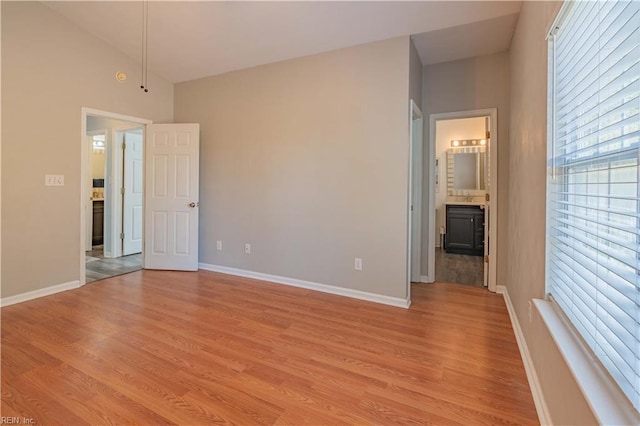 unfurnished bedroom with light wood-style floors, baseboards, and vaulted ceiling