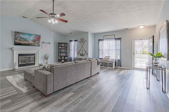 living area featuring a glass covered fireplace, visible vents, baseboards, and wood finished floors