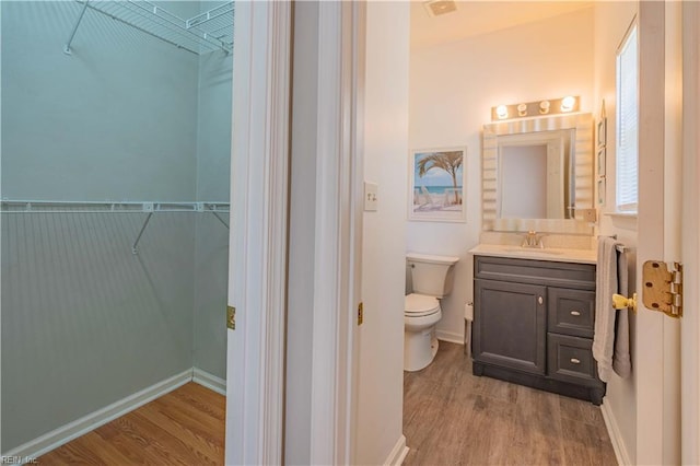 bathroom with wood finished floors, toilet, and a walk in closet