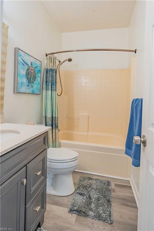 full bath featuring toilet, wood finished floors, vanity, and shower / tub combo with curtain