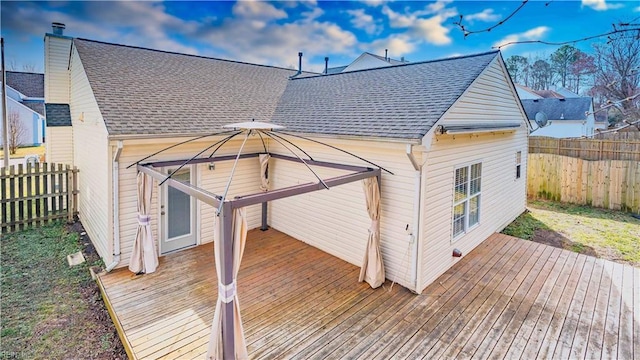 rear view of property with a chimney, roof with shingles, fence, and a deck