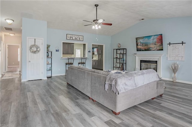 living room with baseboards, visible vents, a glass covered fireplace, lofted ceiling, and wood finished floors