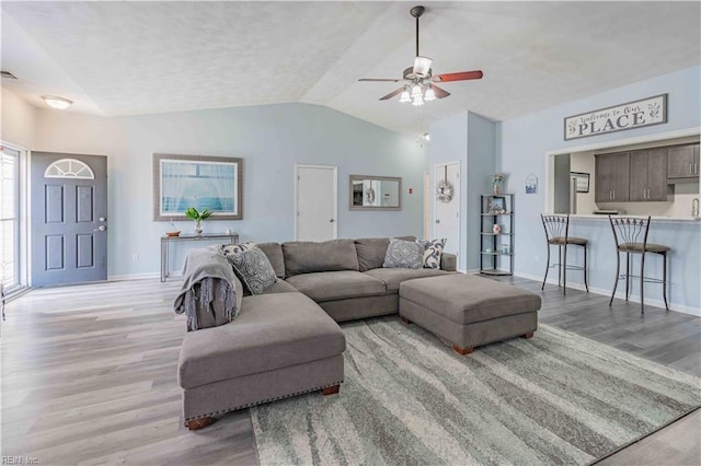 living area featuring lofted ceiling, baseboards, and light wood finished floors