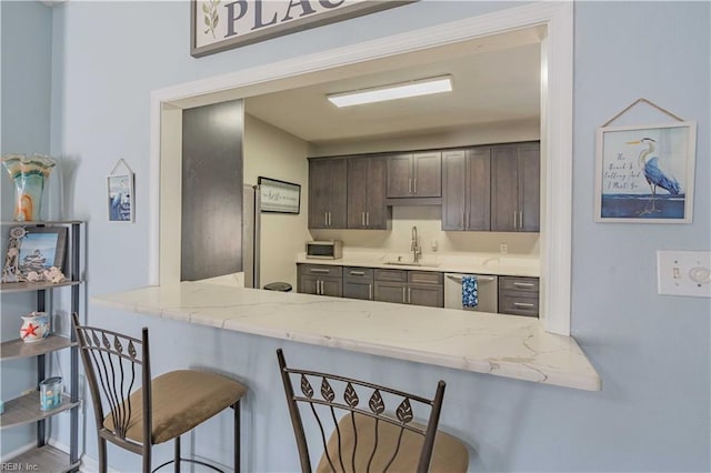 kitchen featuring a sink, dark brown cabinetry, stainless steel dishwasher, and light stone countertops