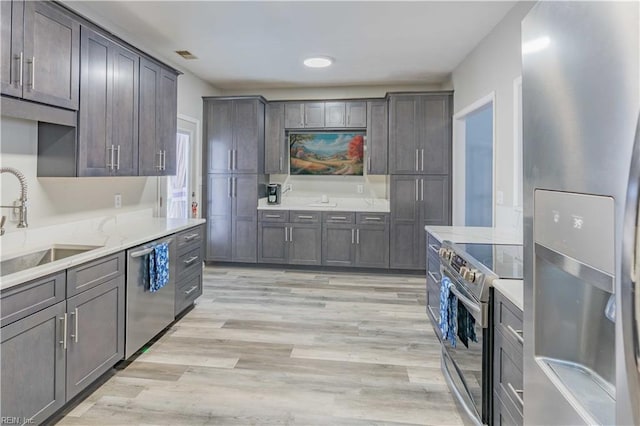 kitchen with stainless steel appliances, light wood finished floors, a sink, and dark brown cabinets