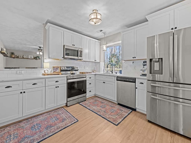 kitchen featuring stainless steel appliances, a sink, white cabinets, light wood-style floors, and light countertops