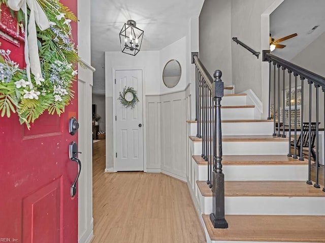 foyer entrance with ceiling fan with notable chandelier, stairway, and wood finished floors