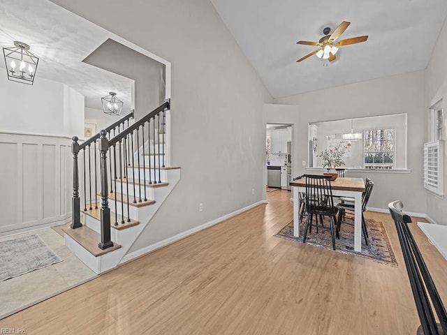 dining room with ceiling fan with notable chandelier, lofted ceiling, stairway, and wood finished floors