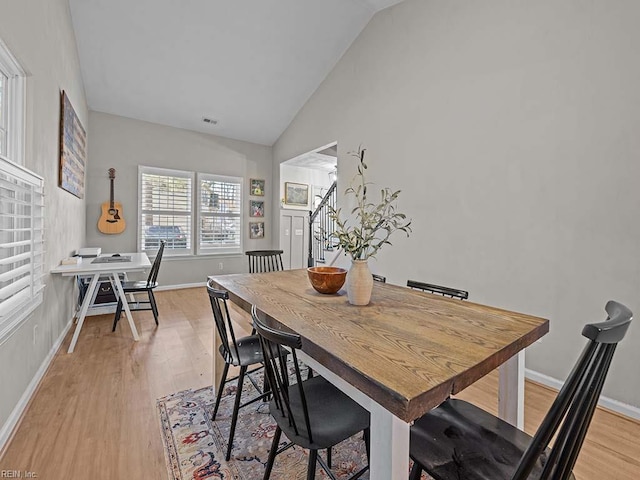 dining room with visible vents, light wood-style flooring, vaulted ceiling, baseboards, and stairs