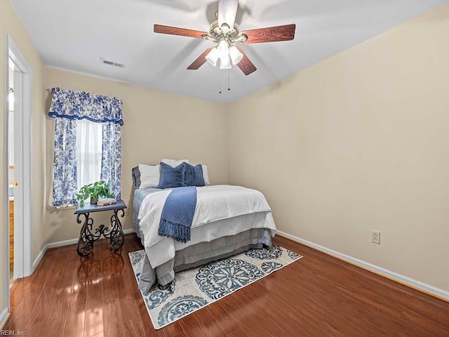 bedroom with a ceiling fan, visible vents, baseboards, and wood finished floors