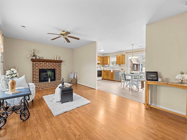 living area featuring a fireplace, visible vents, baseboards, a ceiling fan, and light wood-type flooring