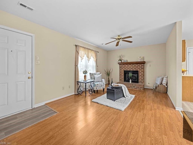 living room featuring light wood-style flooring, visible vents, baseboards, a ceiling fan, and a brick fireplace