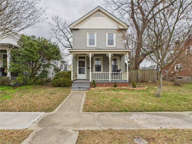 victorian house with covered porch, fence, and a front lawn