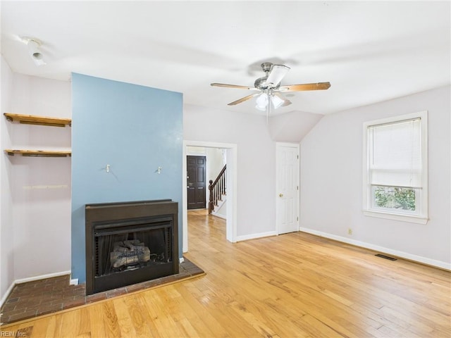 unfurnished living room with visible vents, a fireplace with raised hearth, hardwood / wood-style floors, ceiling fan, and baseboards