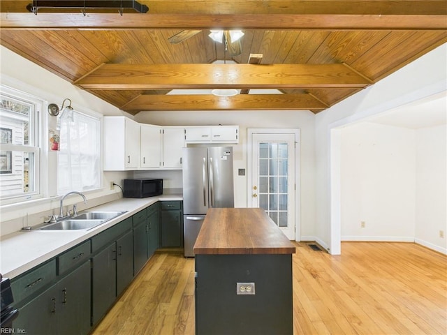 kitchen with black microwave, butcher block counters, a sink, light wood-type flooring, and freestanding refrigerator