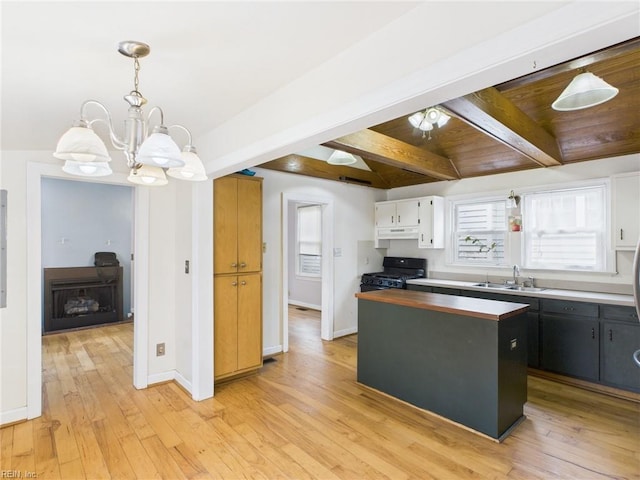 kitchen featuring light wood-style flooring, under cabinet range hood, a sink, beam ceiling, and black gas range oven