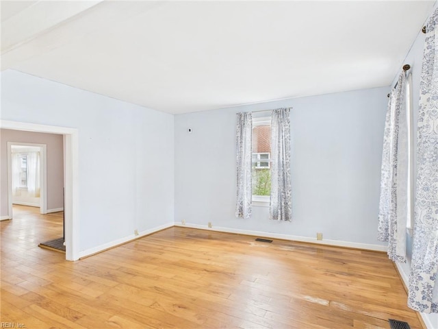 empty room with baseboards, light wood-style flooring, visible vents, and a wealth of natural light