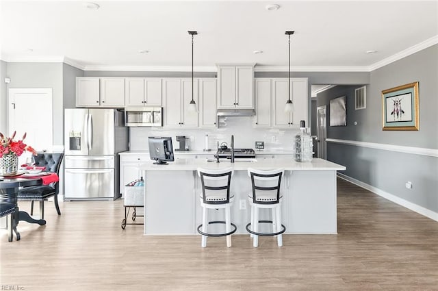 kitchen with a breakfast bar, light countertops, under cabinet range hood, appliances with stainless steel finishes, and backsplash