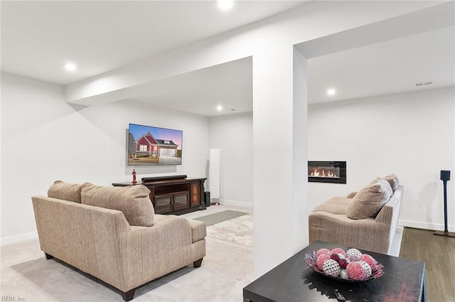 living area featuring a glass covered fireplace, recessed lighting, visible vents, and baseboards