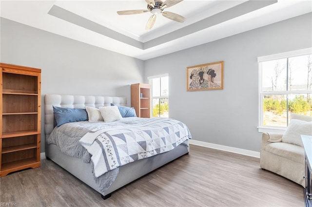 bedroom featuring a raised ceiling, wood finished floors, baseboards, and ceiling fan