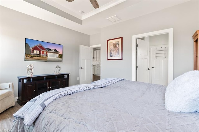 bedroom with a tray ceiling, visible vents, wood finished floors, and ceiling fan