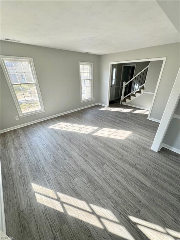 unfurnished living room featuring dark wood-style floors, baseboards, and stairway