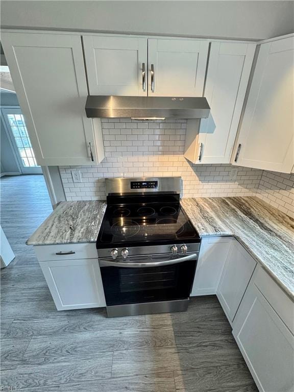 kitchen with light stone counters, tasteful backsplash, white cabinetry, under cabinet range hood, and stainless steel electric range