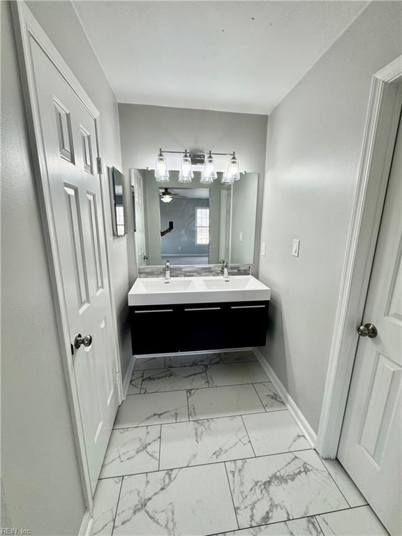 full bath with double vanity, marble finish floor, baseboards, and a sink