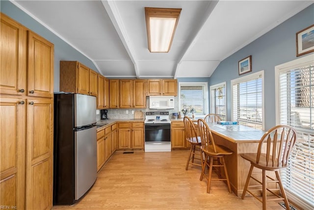 kitchen with white appliances, tile countertops, lofted ceiling, a breakfast bar area, and a healthy amount of sunlight