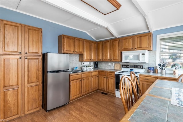 kitchen featuring tile countertops, vaulted ceiling with beams, white appliances, a sink, and wood finished floors