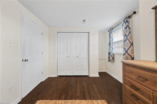 unfurnished bedroom featuring a closet, dark wood finished floors, visible vents, and baseboards