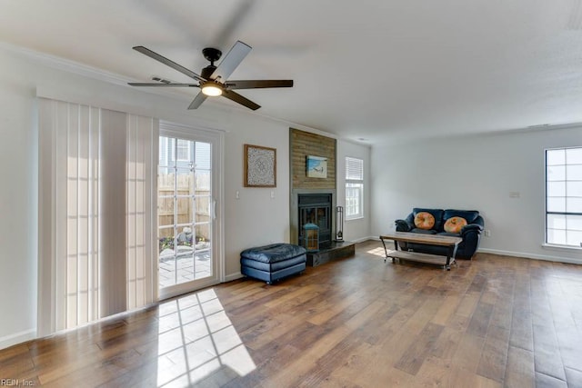 living room featuring a large fireplace, baseboards, ceiling fan, wood finished floors, and crown molding